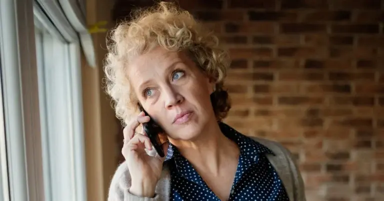 A woman looks concerned while on the phone by a window