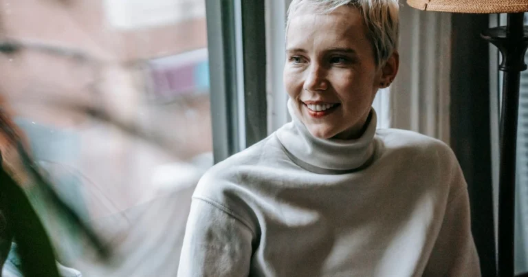 Smiling woman looking out a window, feeling hopeful and informed