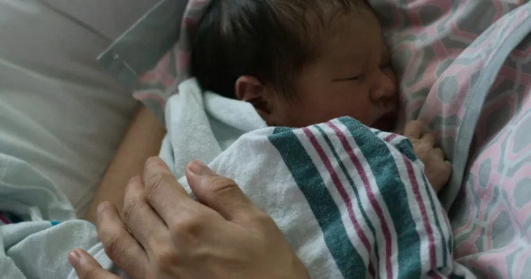 Newborn sleeping in a striped hospital blanket in a parent's arms