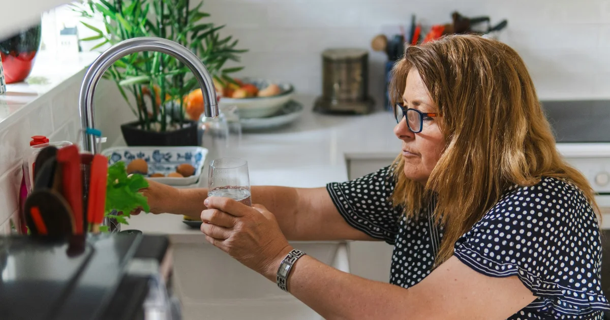 Woman in her 50s filling a glass of water at the kitchen sink