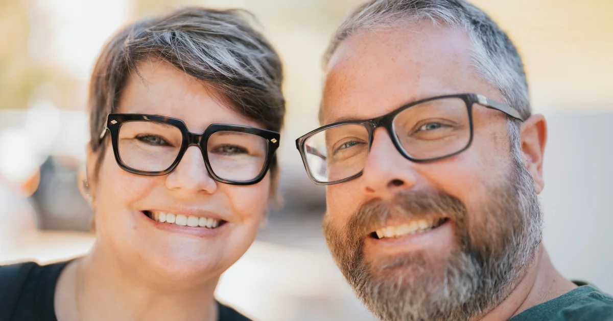 Smiling couple in their forties with glasses posing cheek to cheek outdoors