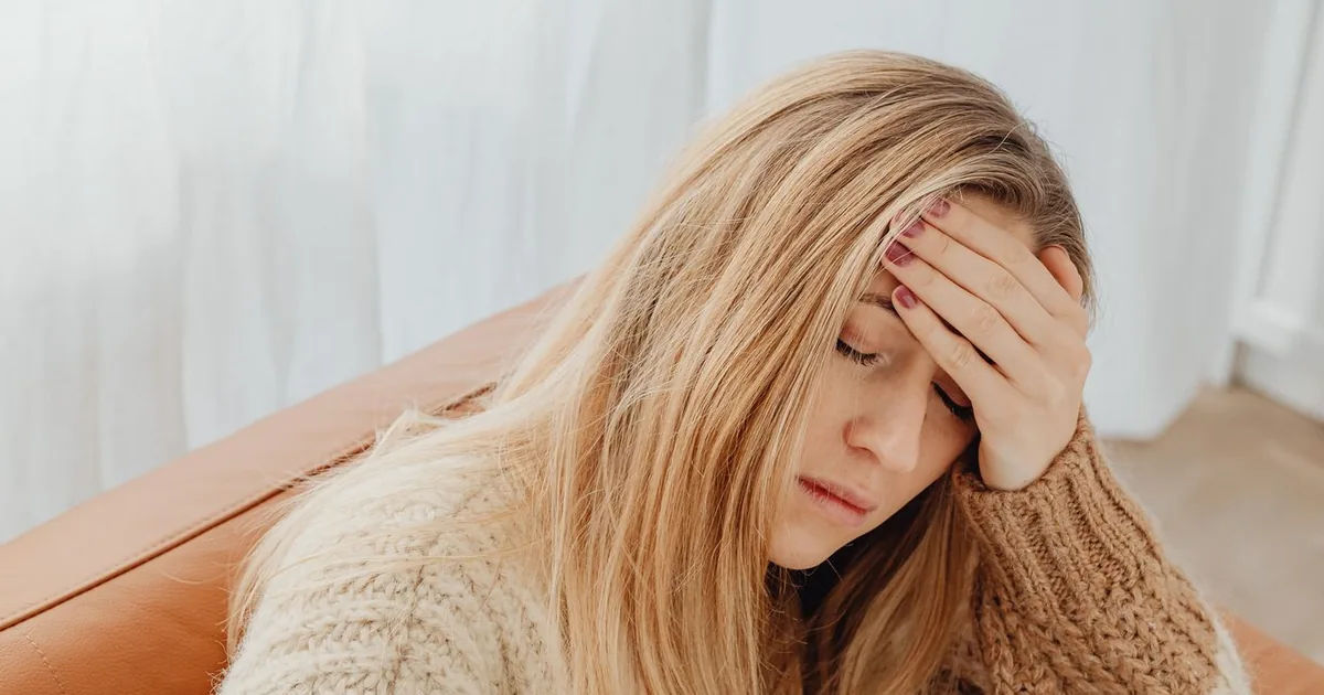 Woman sitting on a sofa with her eyes closed and her hand pressed to her forehead